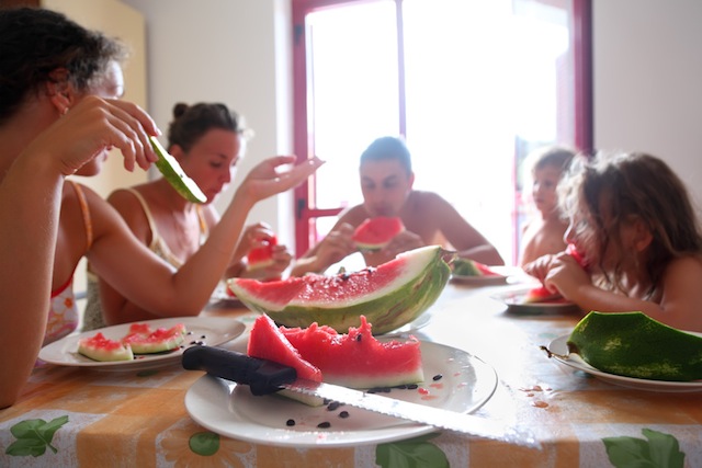 family eats juicy watermelon. Focus on plate with piece of watermelon and knife